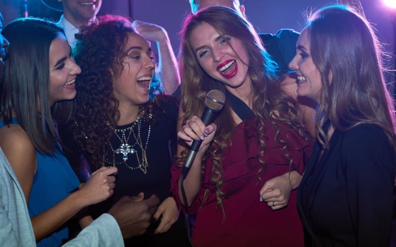 A group of people playfully singing into a microphone at a party.